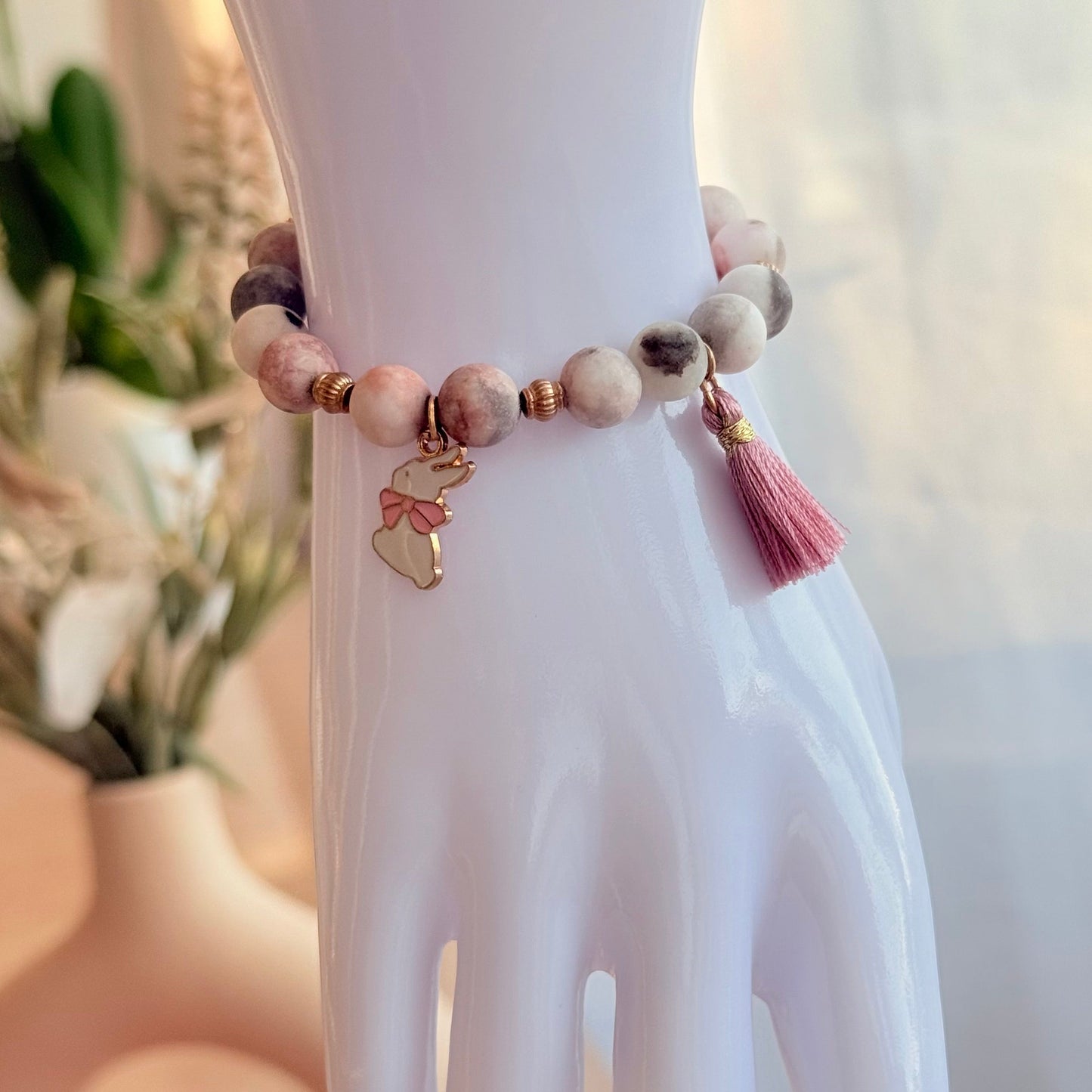 Handgefertigtes Natursteinarmband mit Hasen-Anhänger und rosa Quaste auf Stein