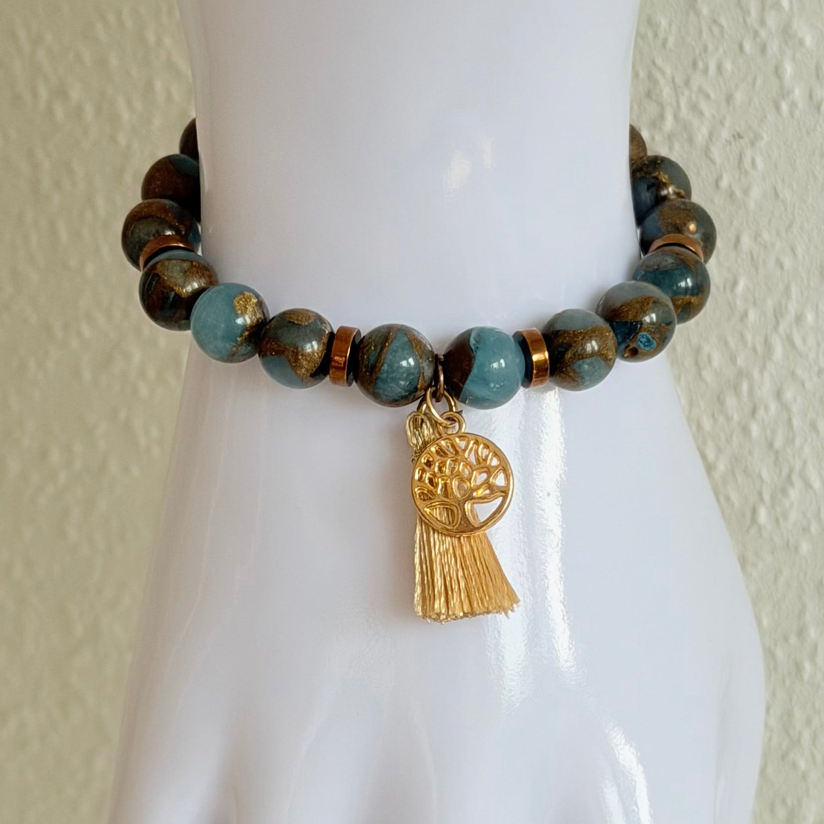 Handgefertigtes Naturstein-Armband in Blau- und Erdtönen mit Lebensbaum-Anhänger am Handgelenk